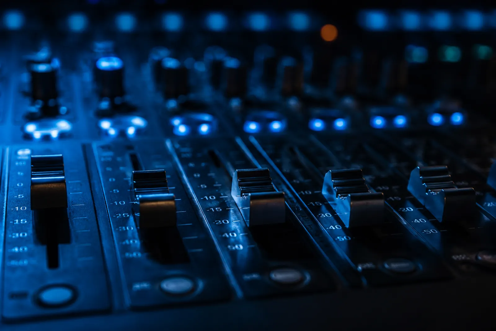 Close-up of the faders on a mixing console lit in blue.